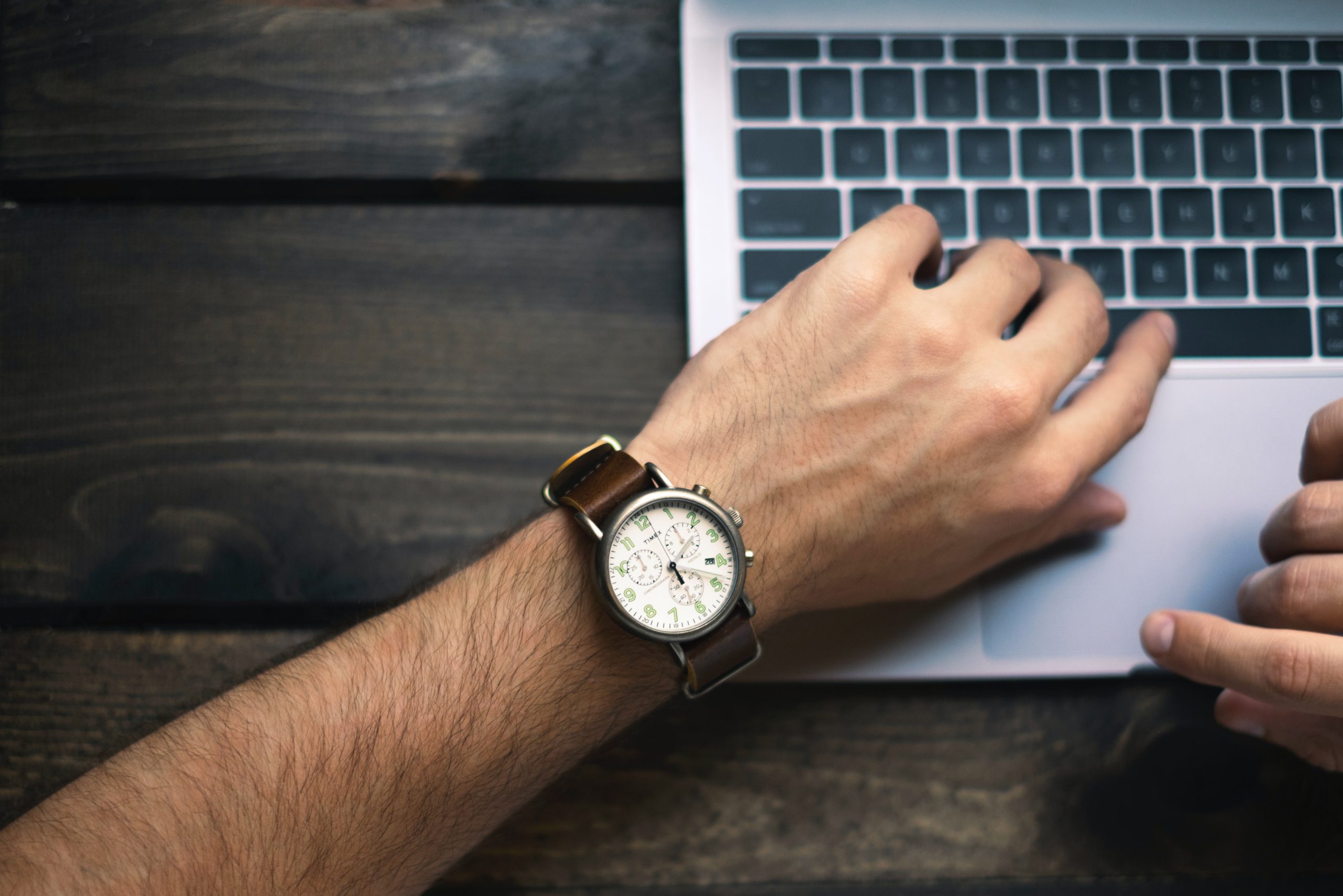 A project manager on their computer looking at their watch keeping careful eye on their time management