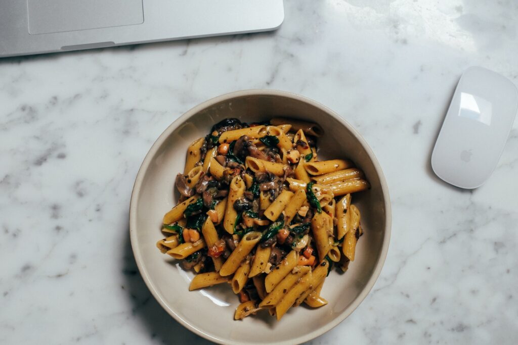 a desk with a laptop and a mouse as well as a plate full of food for lunch