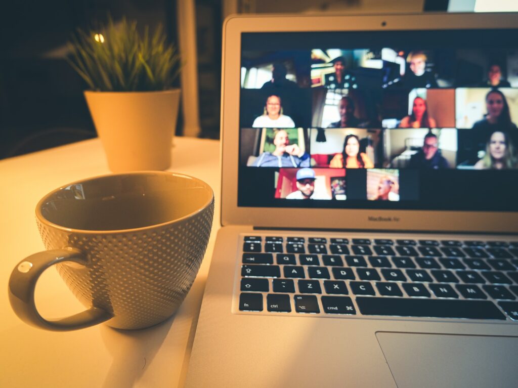 a group of colleagues doing a virtual summer team building activity together on a laptop at a desk on zoom with a cup of coffee