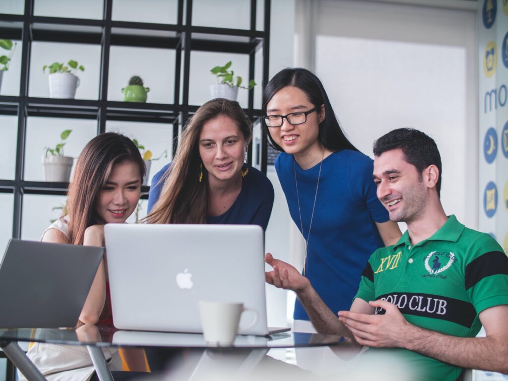 four colleagues sitting around a macbook in their office looking at something on the screen
