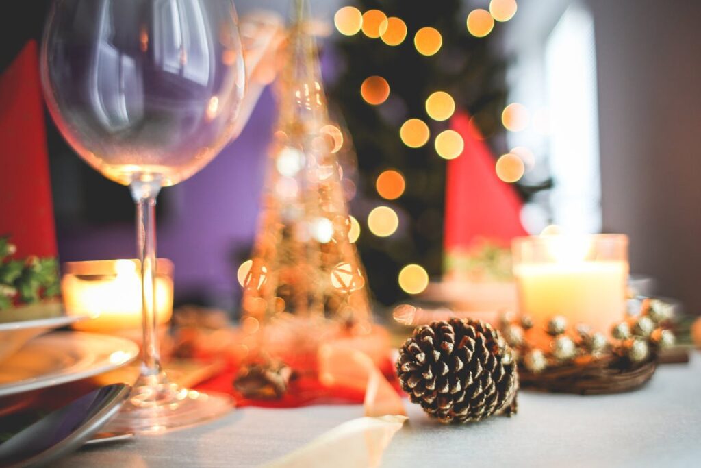 Holiday dinner table setting with pine cone, candle, wine glass and Christmas lights
