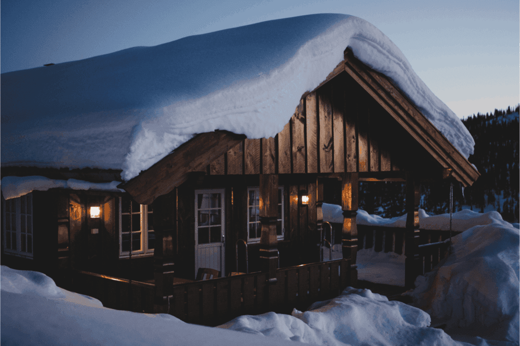 Rustic wooden cabin nestled in deep snow, glowing with warm lights at dusk