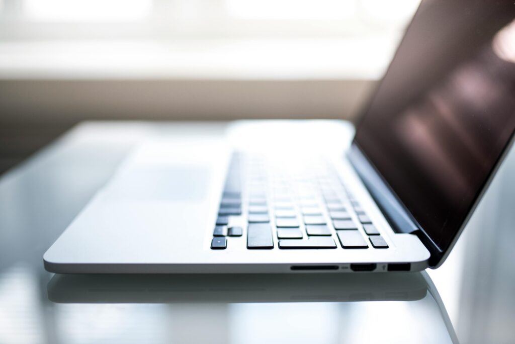 Close-up of a sleek laptop on a glass desk in natural light – remote work setup, minimalist workspace, digital productivity, modern technology