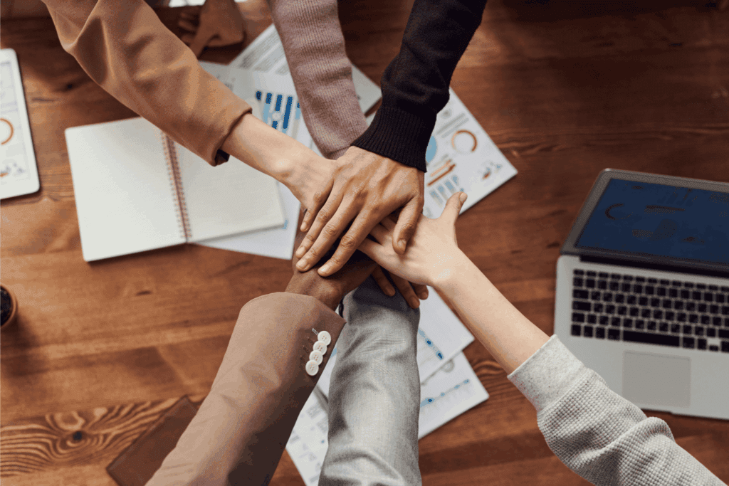 Diverse team stacking hands over business charts and a laptop