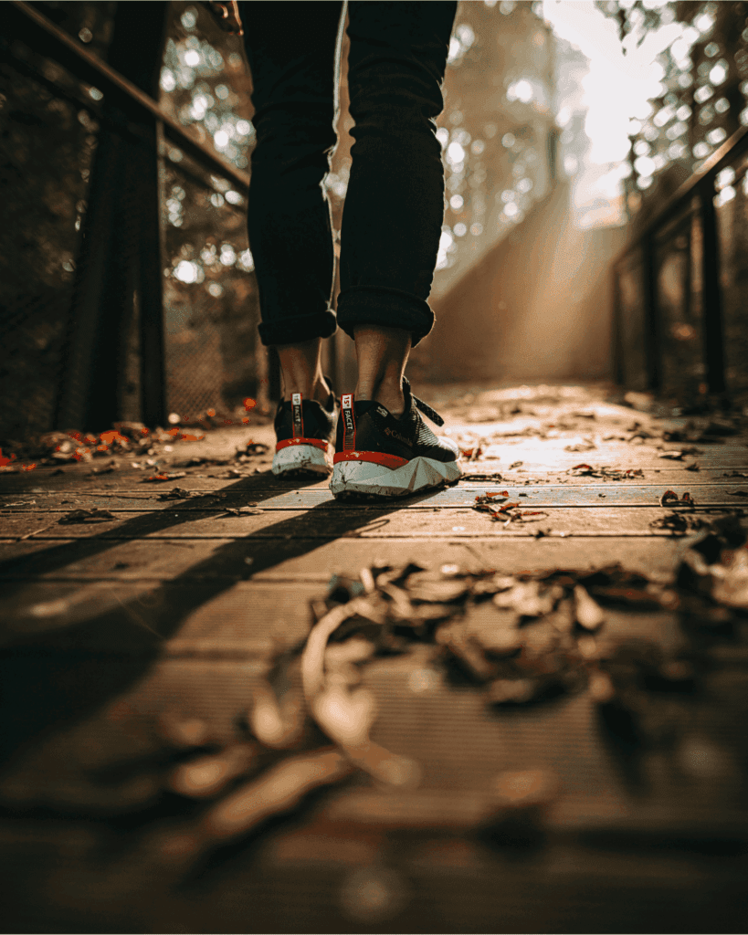 Close-up of a person walking on a wooden path covered in autumn leaves