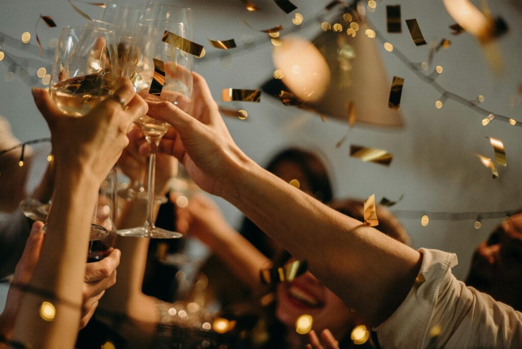 Team members clink glasses in celebration at a festive corporate party with golden confetti and warm lighting