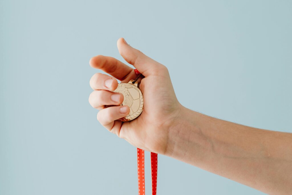 Close-up of a hand holding a gold medal, symbolizing achievement, success, and team recognition