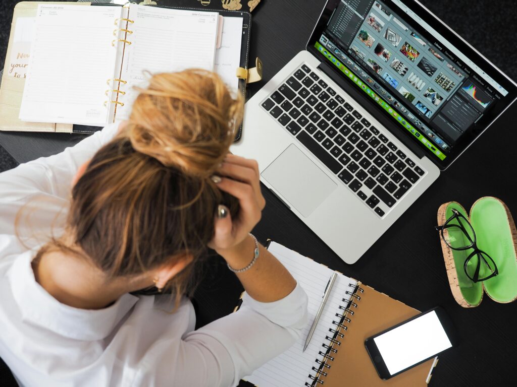 Birdseye view of a stressed employee burying her head in her hands at her cluttered work desk