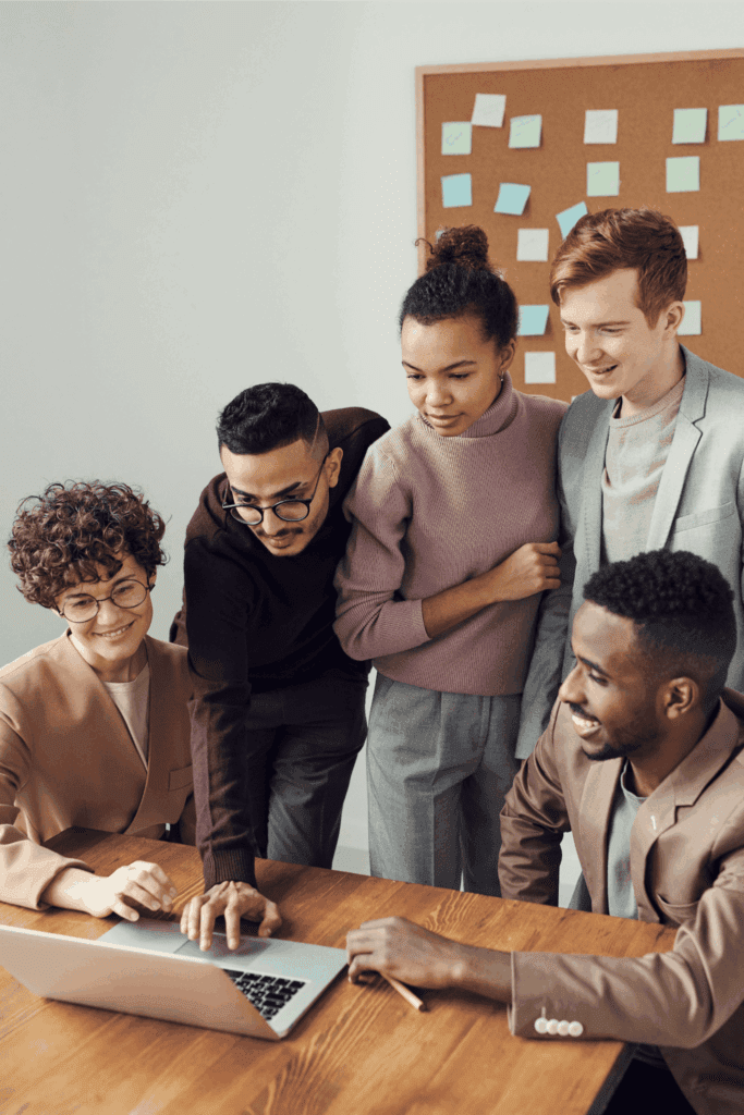 A diverse team of professionals collaborates around a laptop, brainstorming ideas in a modern office setting