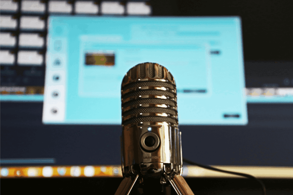 A close-up of a professional podcast microphone with a blurred computer screen in the background, ready for recording