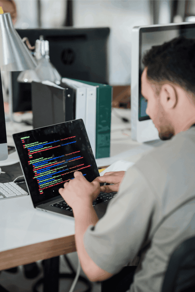A software developer writes and edits code on a laptop while working at a modern office desk.