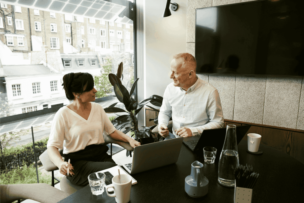 Two business professionals have a productive meeting at a modern office table, discussing ideas with laptops open