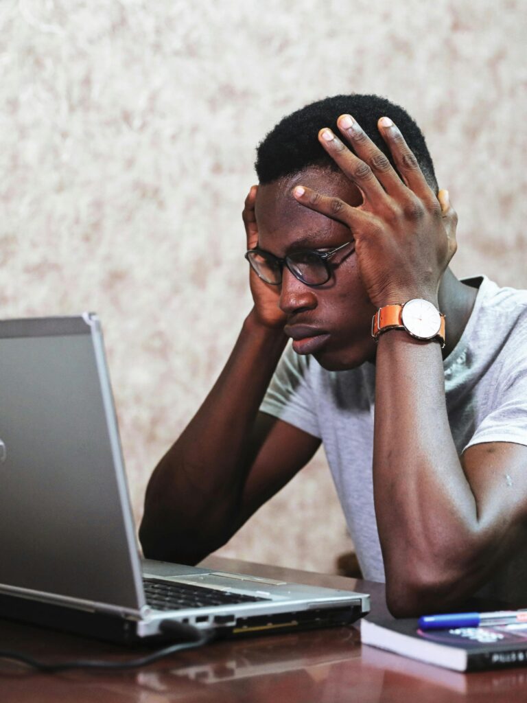 A frustrated man sits at his desk with his hands on his head, staring at his laptop while dealing with work stress