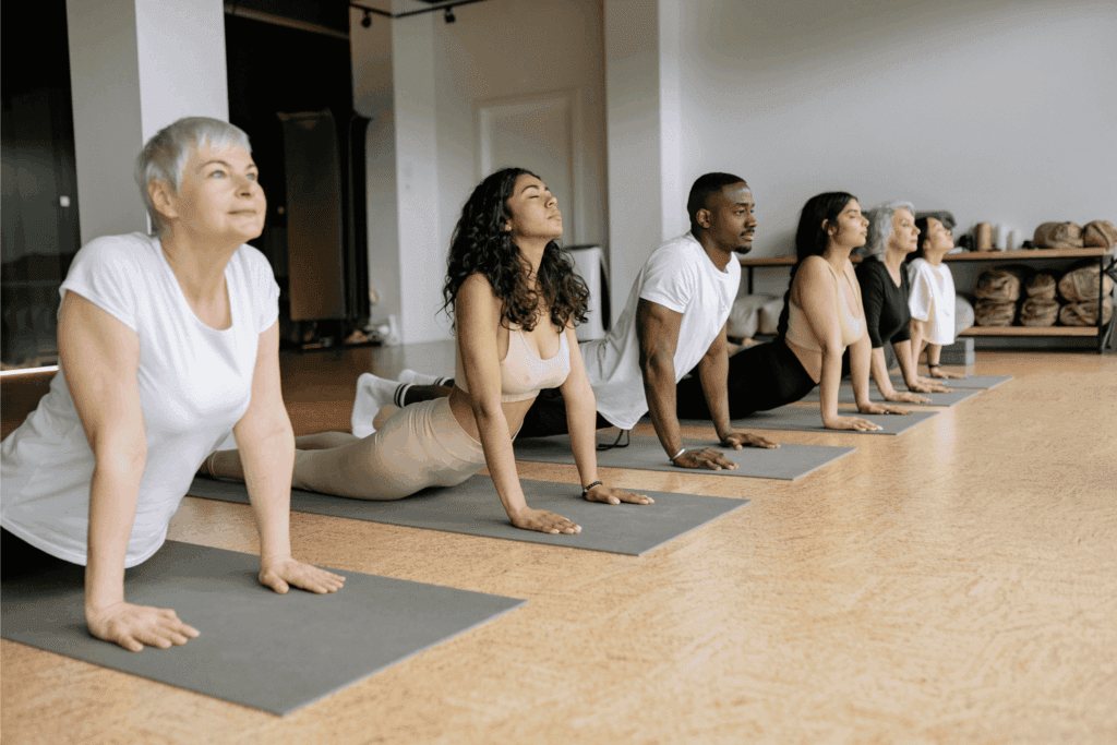 Group of people participates in a yoga class, performing the upward-facing dog pose together on mats, fostering wellness, focus, and community