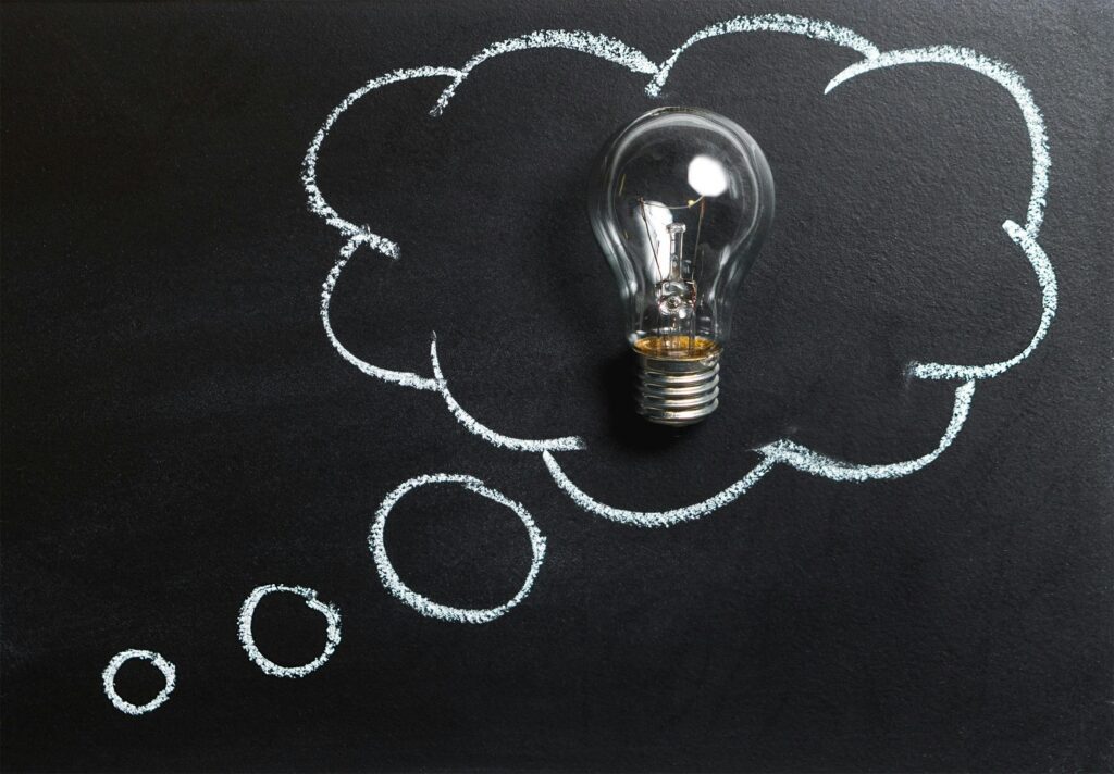 a clear light bulb placed inside a thought bubble drawn in white chalk on a blackboard