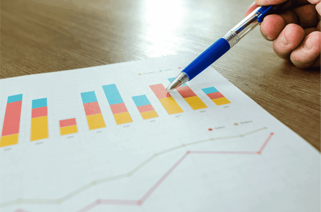 Close-up of a hand pointing at colorful bar and line graphs on a financial report, illustrating sales and order trends.