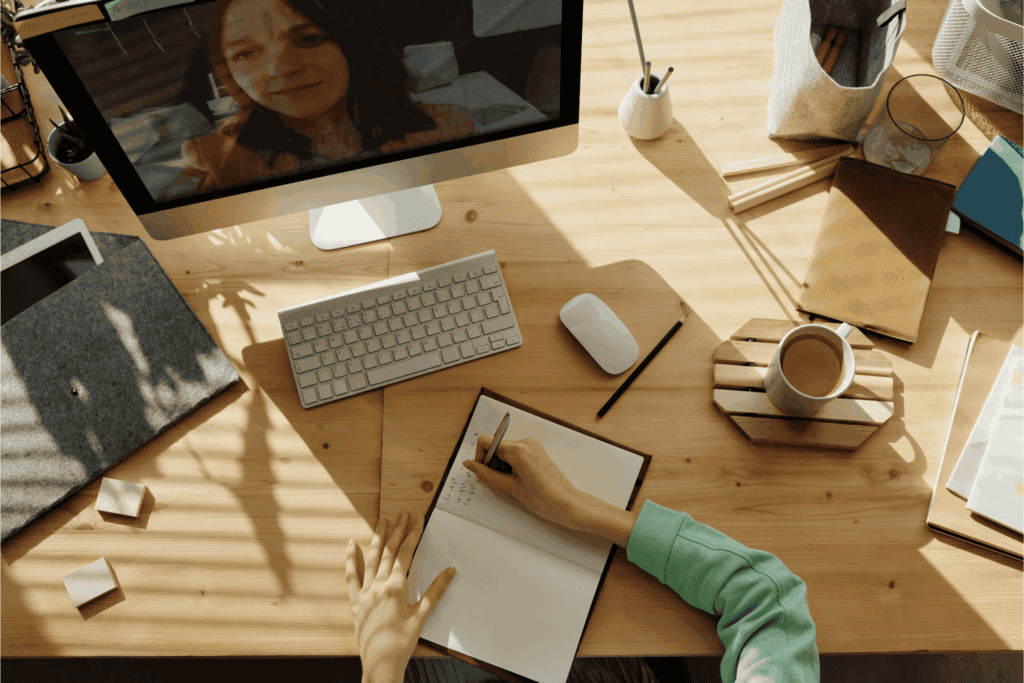Person taking notes during a virtual meeting at a home office desk