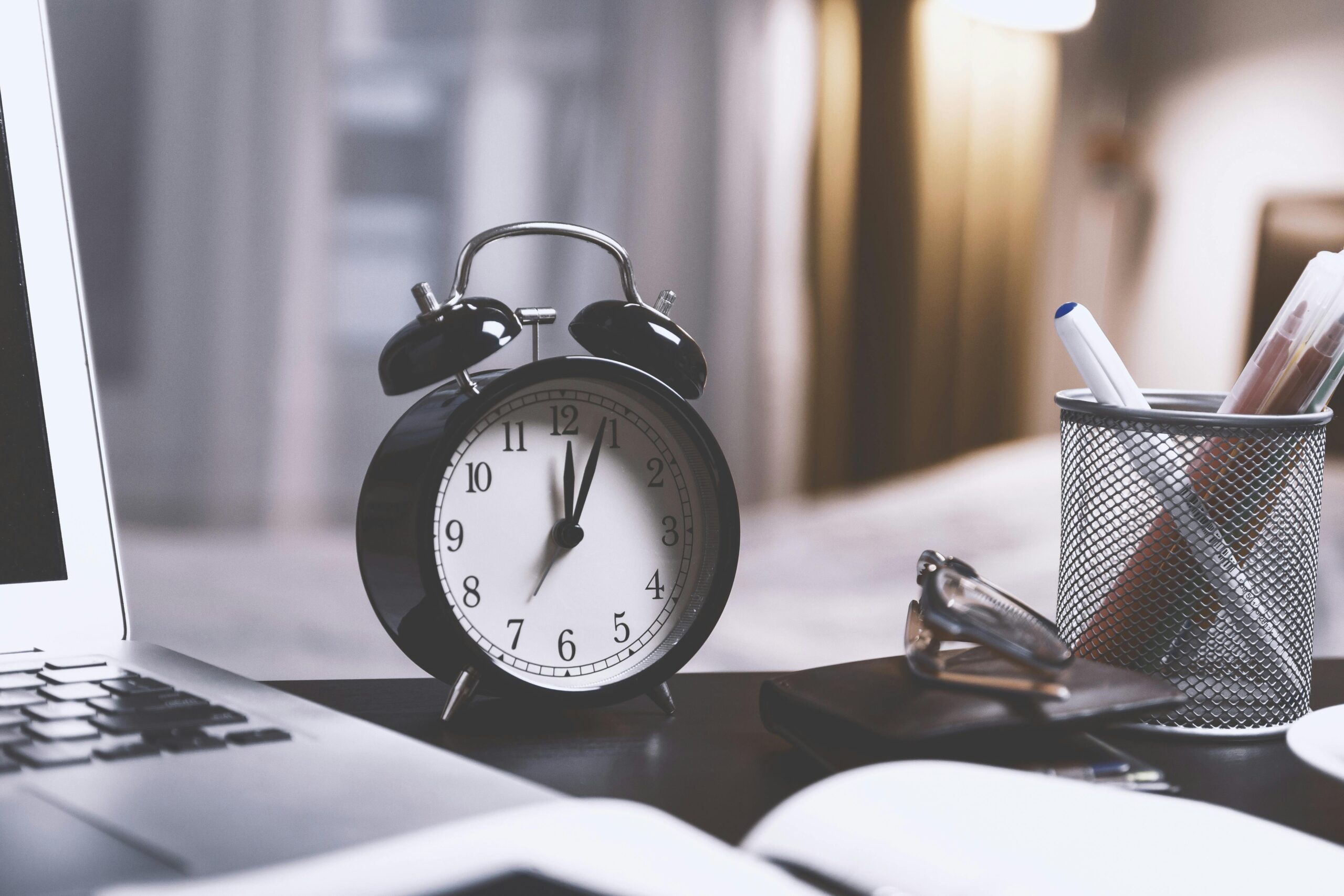 Close-up of a desk clock beside a laptop, symbolizing time management and productivity in remote work.