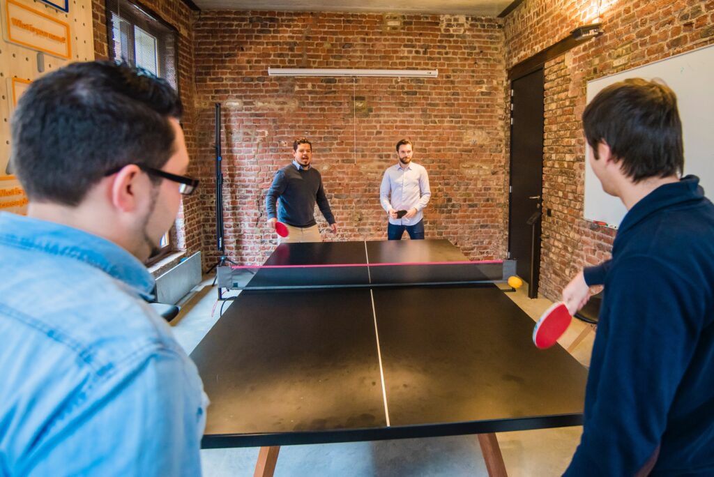 four employees playing ping pong in the office as they enjoy a relaxing employee benefit