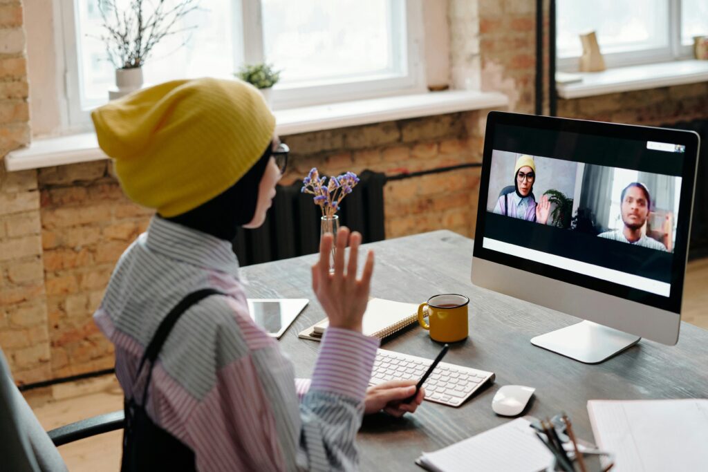 Person participating in a virtual meeting, waving at colleagues on a video call from a modern home office workspace