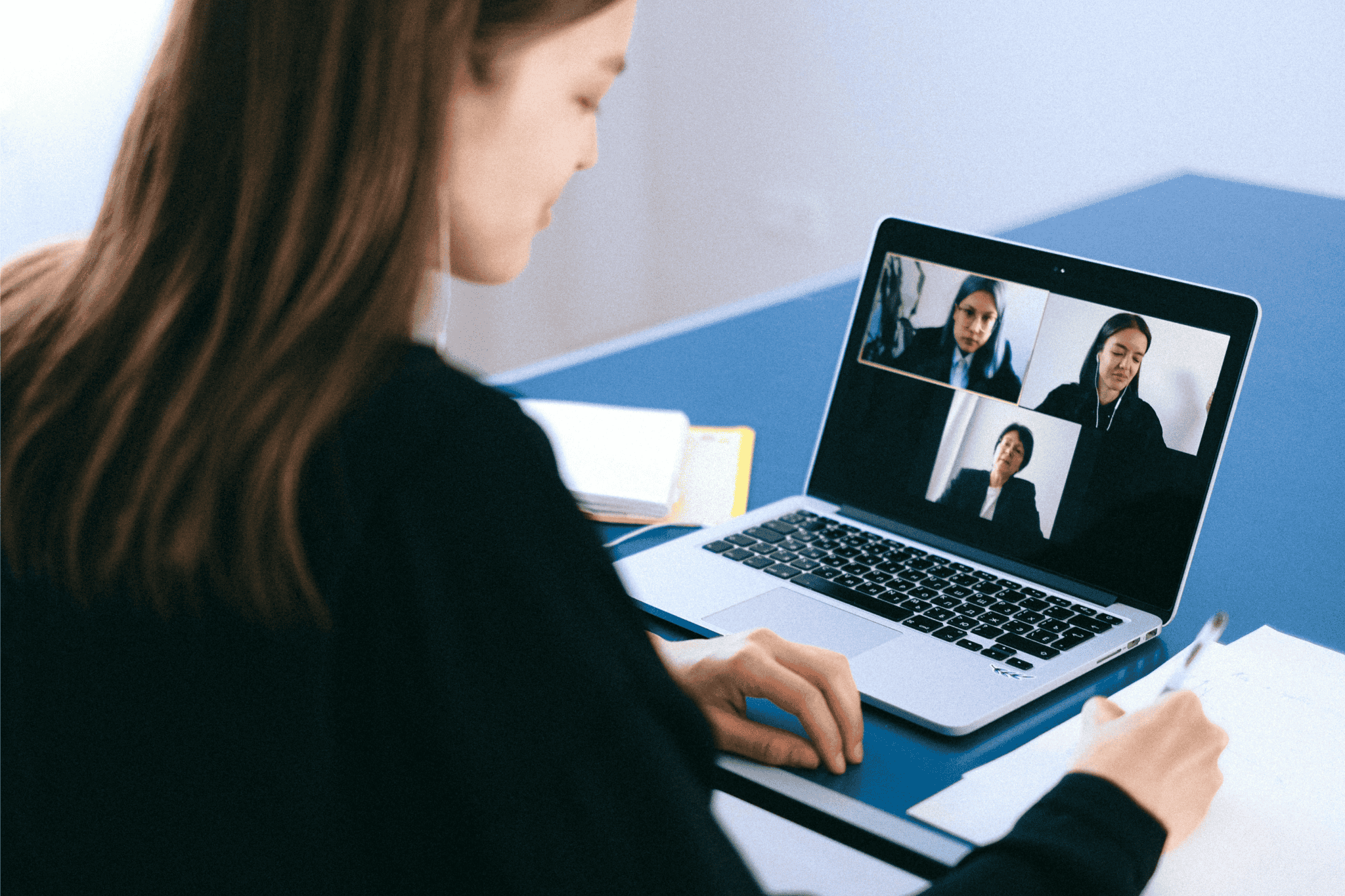 Woman attending an online meeting on laptop while taking notes