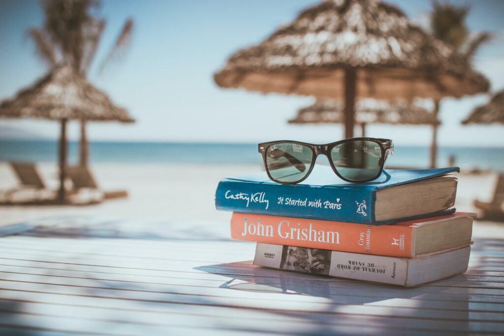 a stack of books and some glasses that someone has taken on holiday to a beach