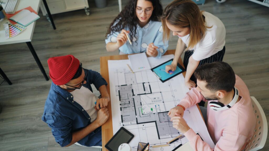 A group of young professionals collaborate over architectural blueprints in a modern office.