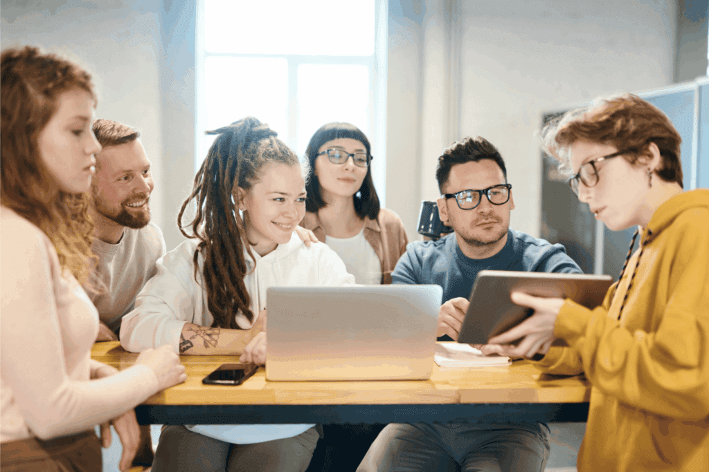 A diverse team collaborates around laptops and tablets, reflecting workplace teamwork.