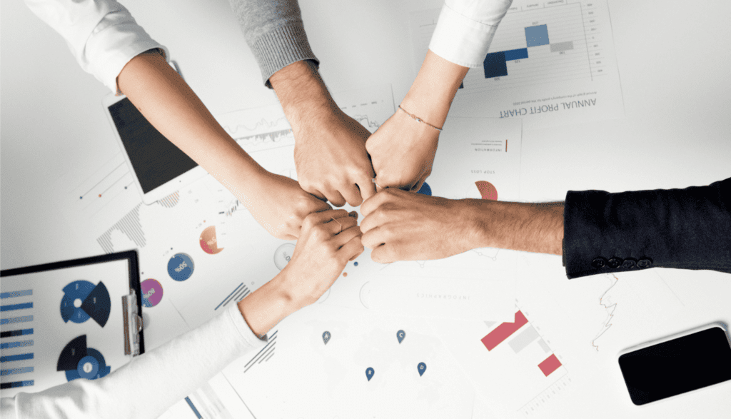 A group of colleagues fist-bump over charts, symbolizing teamwork and success.