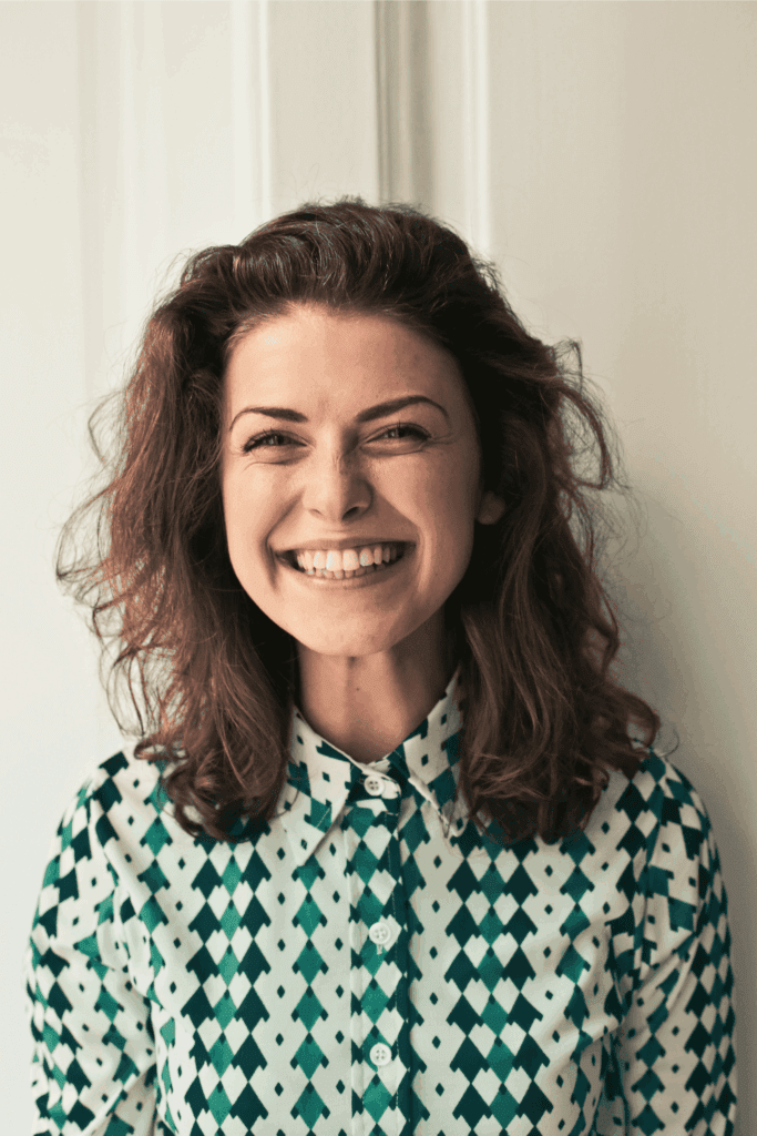 Smiling woman in patterned shirt standing indoors, radiating confidence and happiness