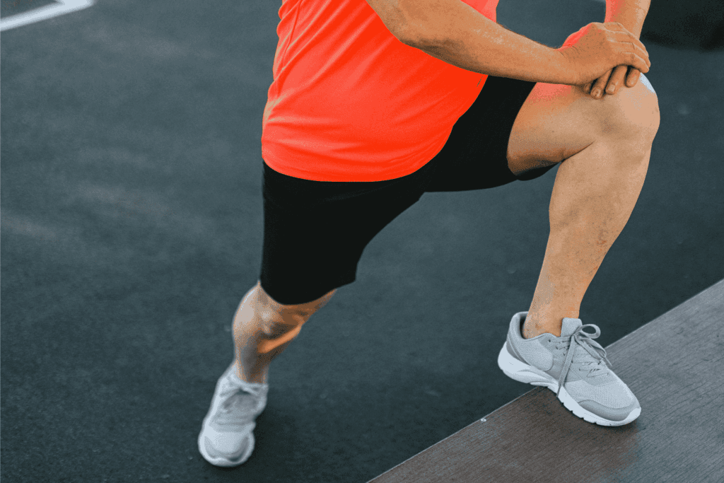 Athlete stretching legs in bright sportswear before workout on outdoor track