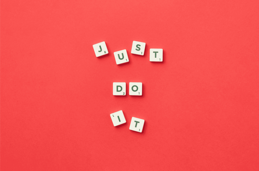 Scrabble letter tiles spelling Just Do It on a bright red background – motivational quote and word game concept.