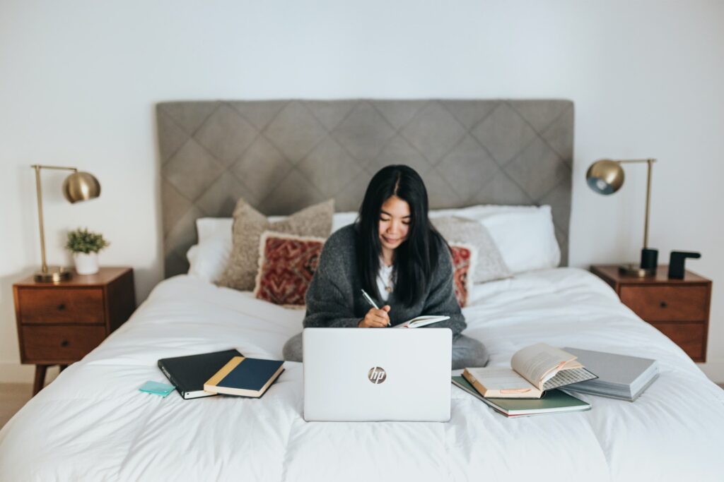 A remote working remote is sitting on her bed, using her laptop to complete work