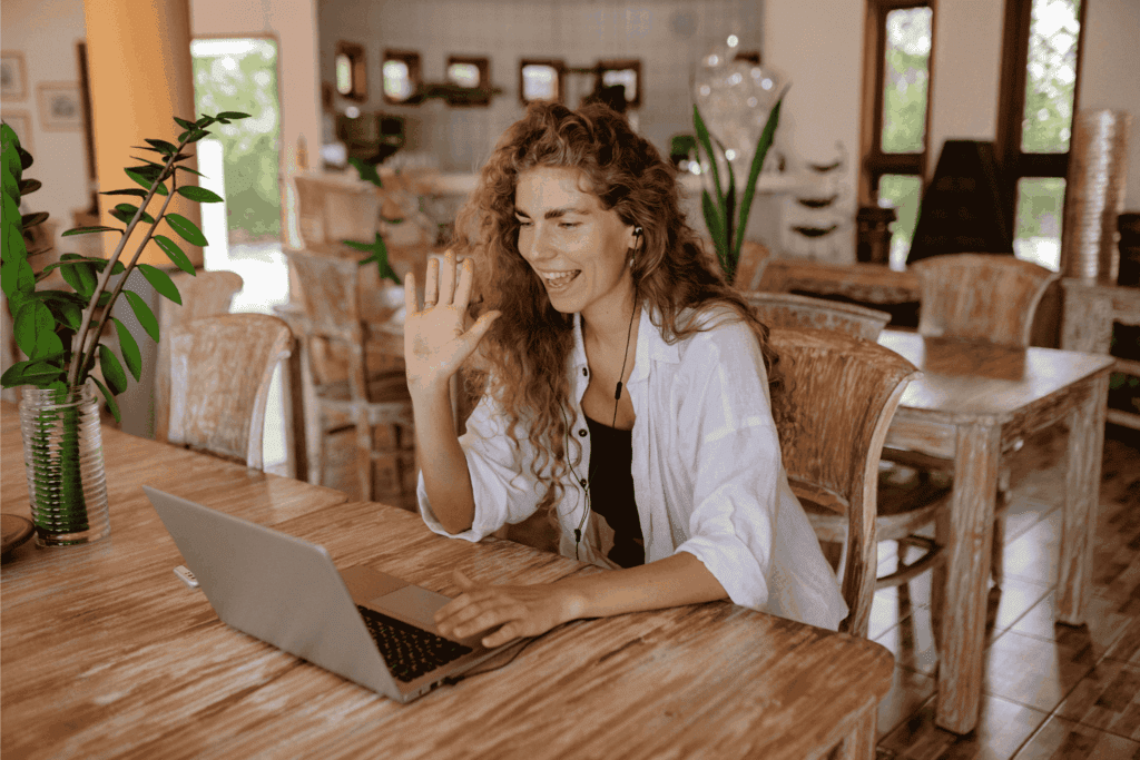 Woman smiling and waving during a video call on her laptop – virtual meeting, remote communication, and online connection concept.