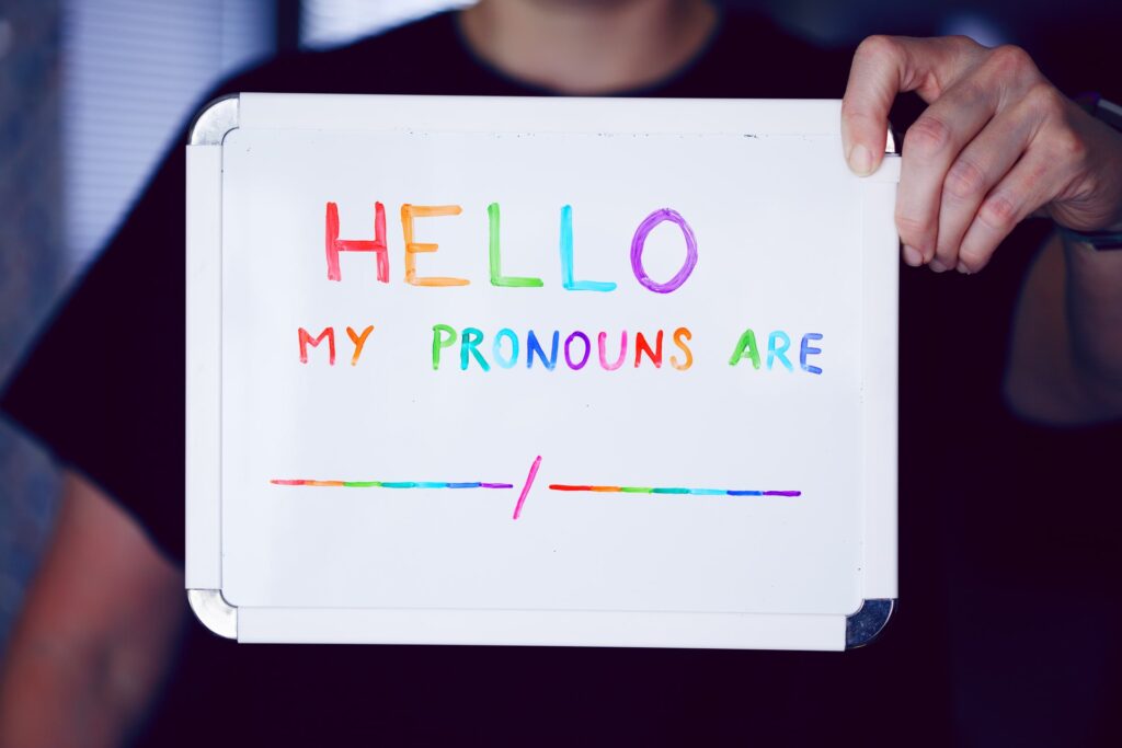 a person holding a whiteboard sign with colorful writing indicating their pronouns