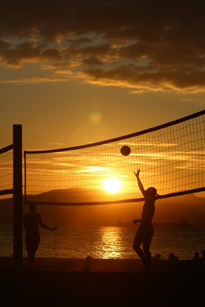 Silhouettes of people playing beach volleyball at sunset – summer sports, outdoor fun, and seaside activity concept.