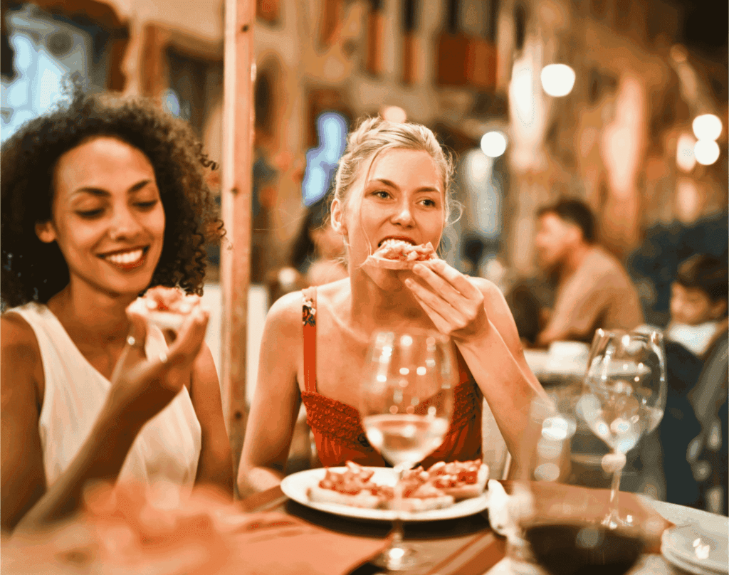 Two women enjoying food and wine at a restaurant – dining out, friendship, and social lifestyle concept.