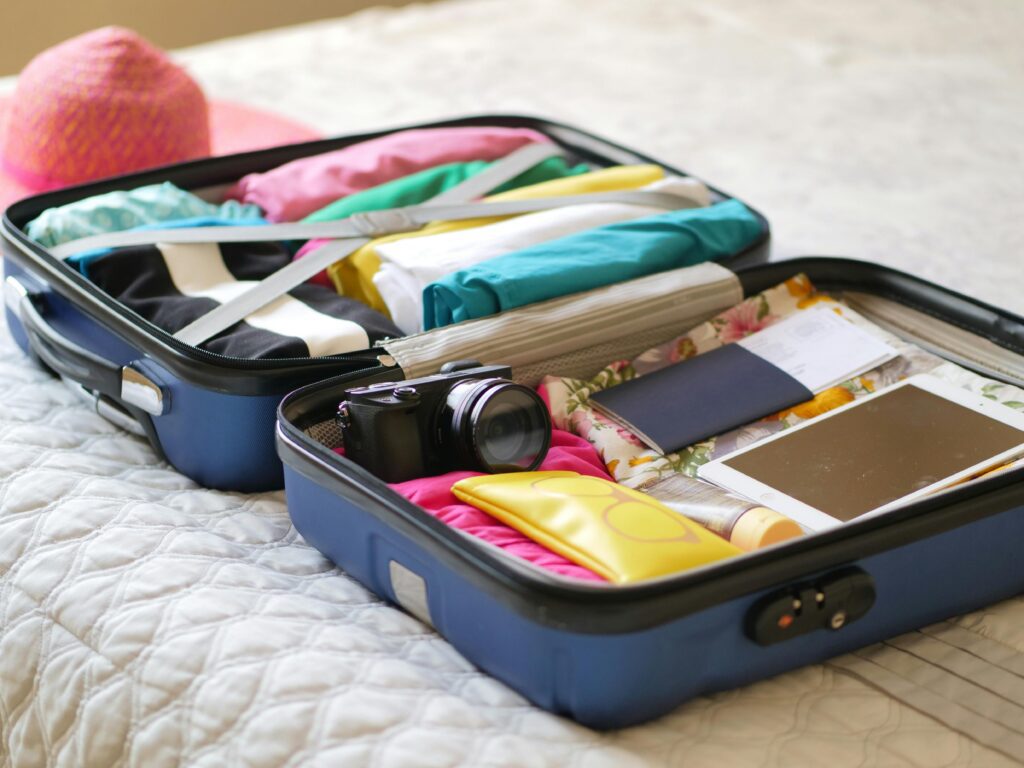 An open suitcase neatly packed with colorful clothes, a camera, a tablet, sunscreen, travel documents, and a passport — symbolizing vacation, travel preparation, or holiday packing.