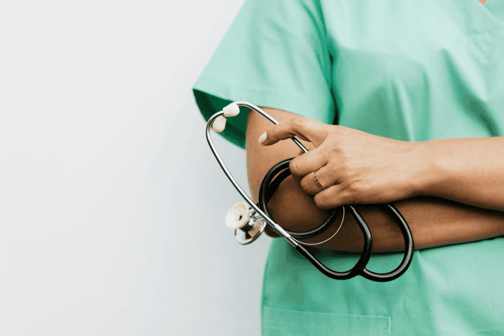 A healthcare professional in green scrubs holds a stethoscope with one hand across their chest, symbolizing care, readiness, and dedication to patient health.
