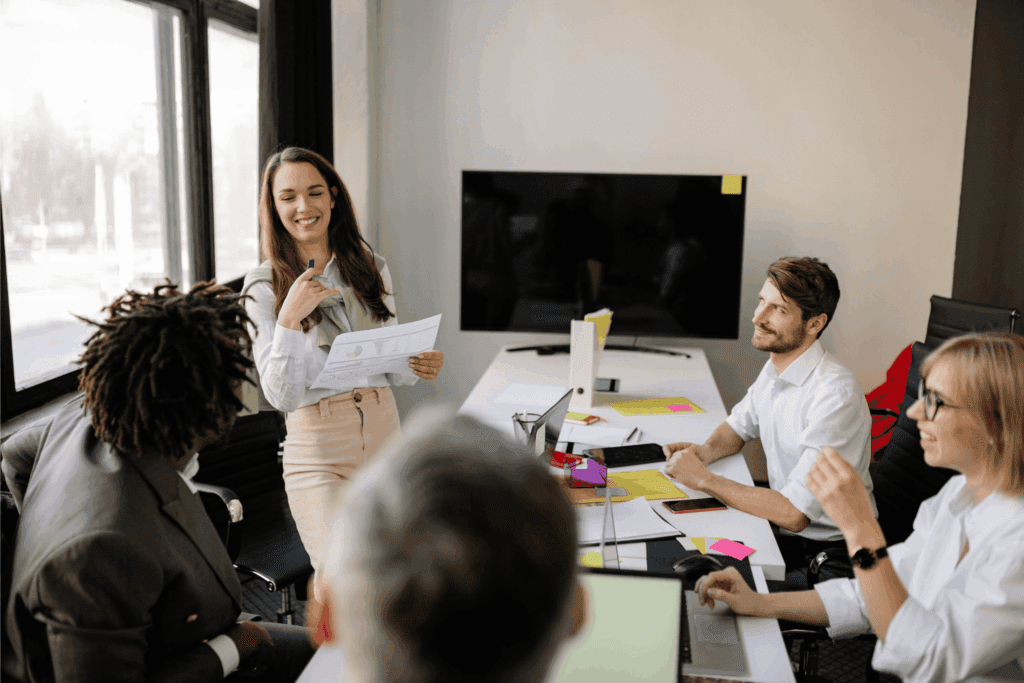 A woman leads a business meeting, presenting documents to colleagues seated around a conference table.