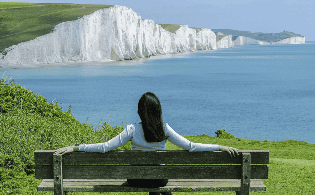 A person sits on a wooden bench overlooking the ocean and the striking white cliffs along the coastline.