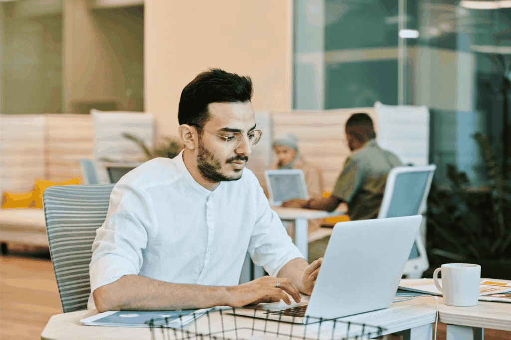 Man in glasses working on a laptop at a modern office desk.
