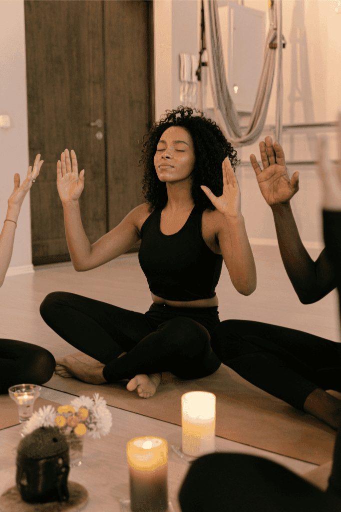 A woman sits cross-legged with eyes closed, meditating in a candlelit yoga class.