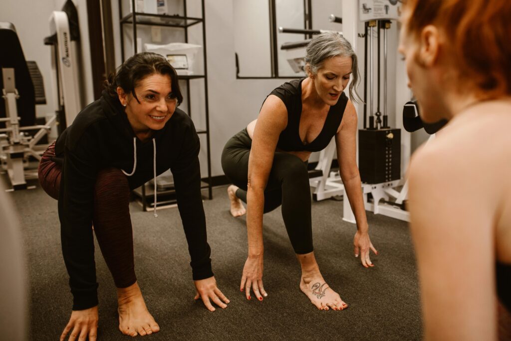 Three women are stretching together in a gym workout session.