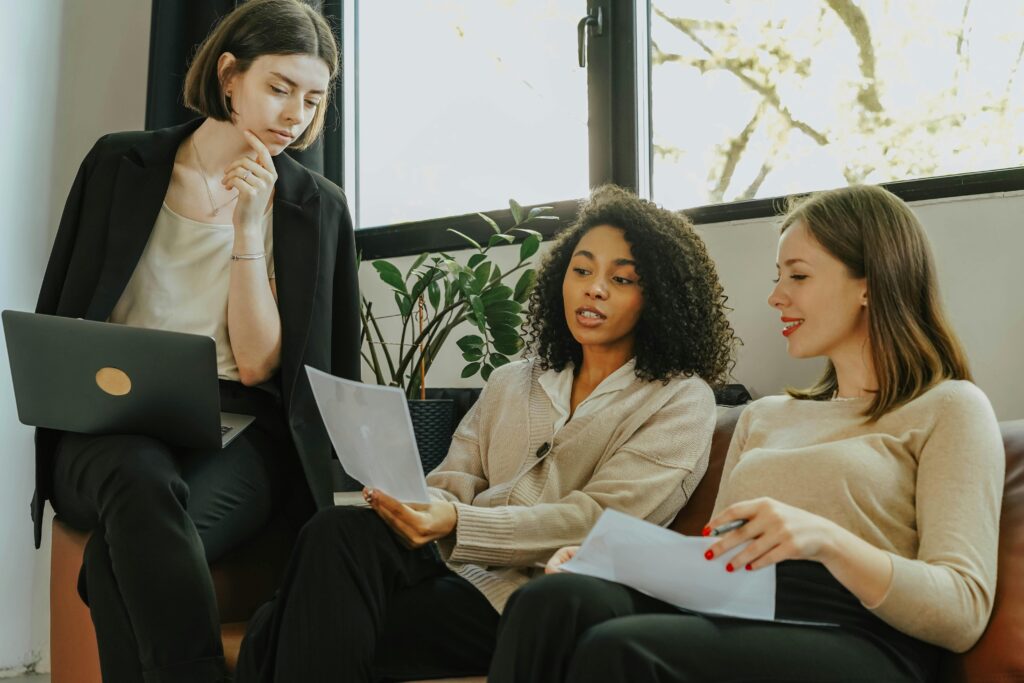 Three women collaborate on documents during a casual business meeting.