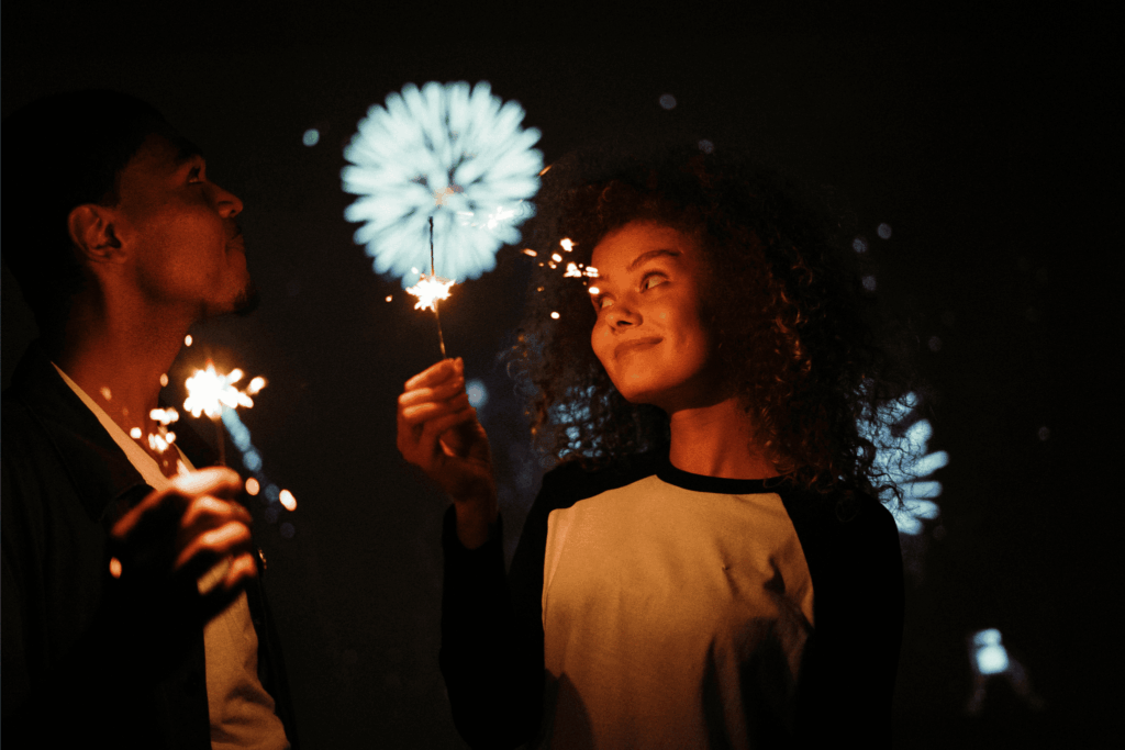 A couple celebrates July 4th with sparklers and fireworks lighting up the night sky.