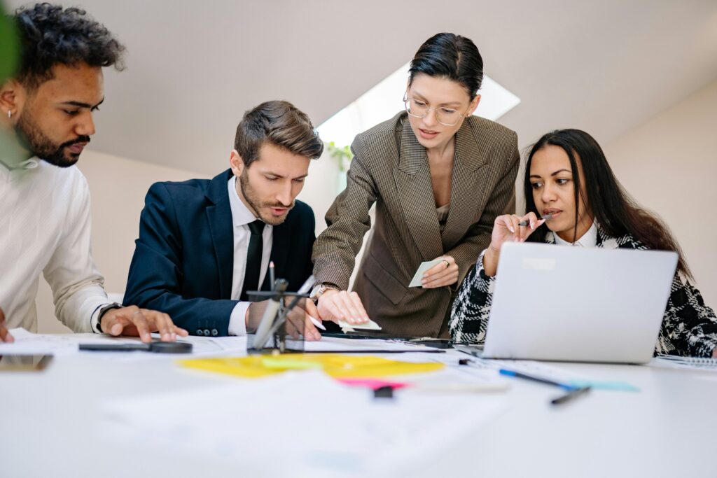 A group of professionals collaborates around a table, reviewing documents and brainstorming ideas together.
