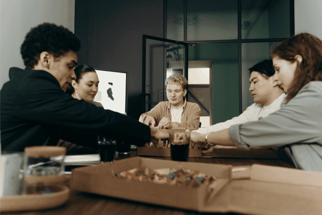 Coworkers share pizza and drinks around a table during an office lunch break.