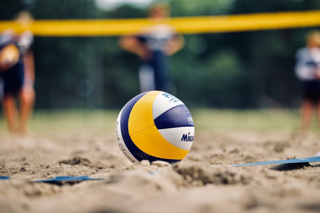 a volleyball laying on the sand at a beach volleyball court with the net in the background