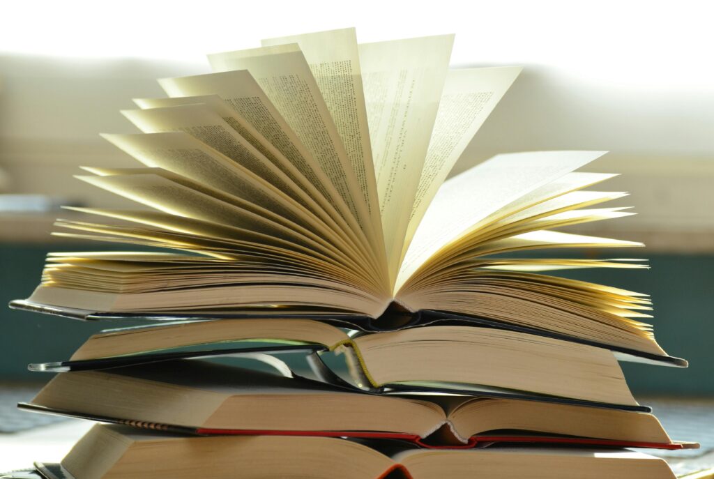An open book with fanned-out pages sits on top of a stack of other books.